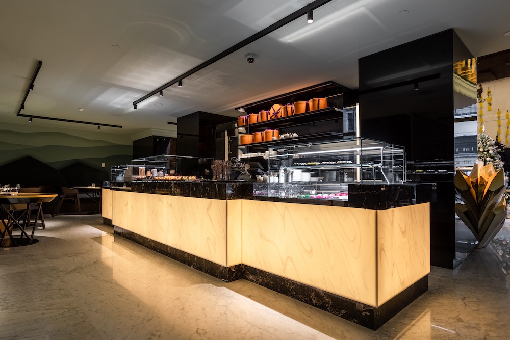 Modern dessert display counter with glass cases, marble and wood accents, filled with pastries and chocolates, set in a sleek, warmly lit restaurant interior.